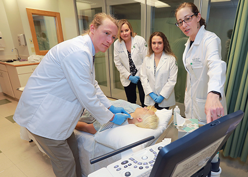 WVSOM faculty member pointing out important information on a ultrasound screen as a student controls the ultrasound on a patients neck 