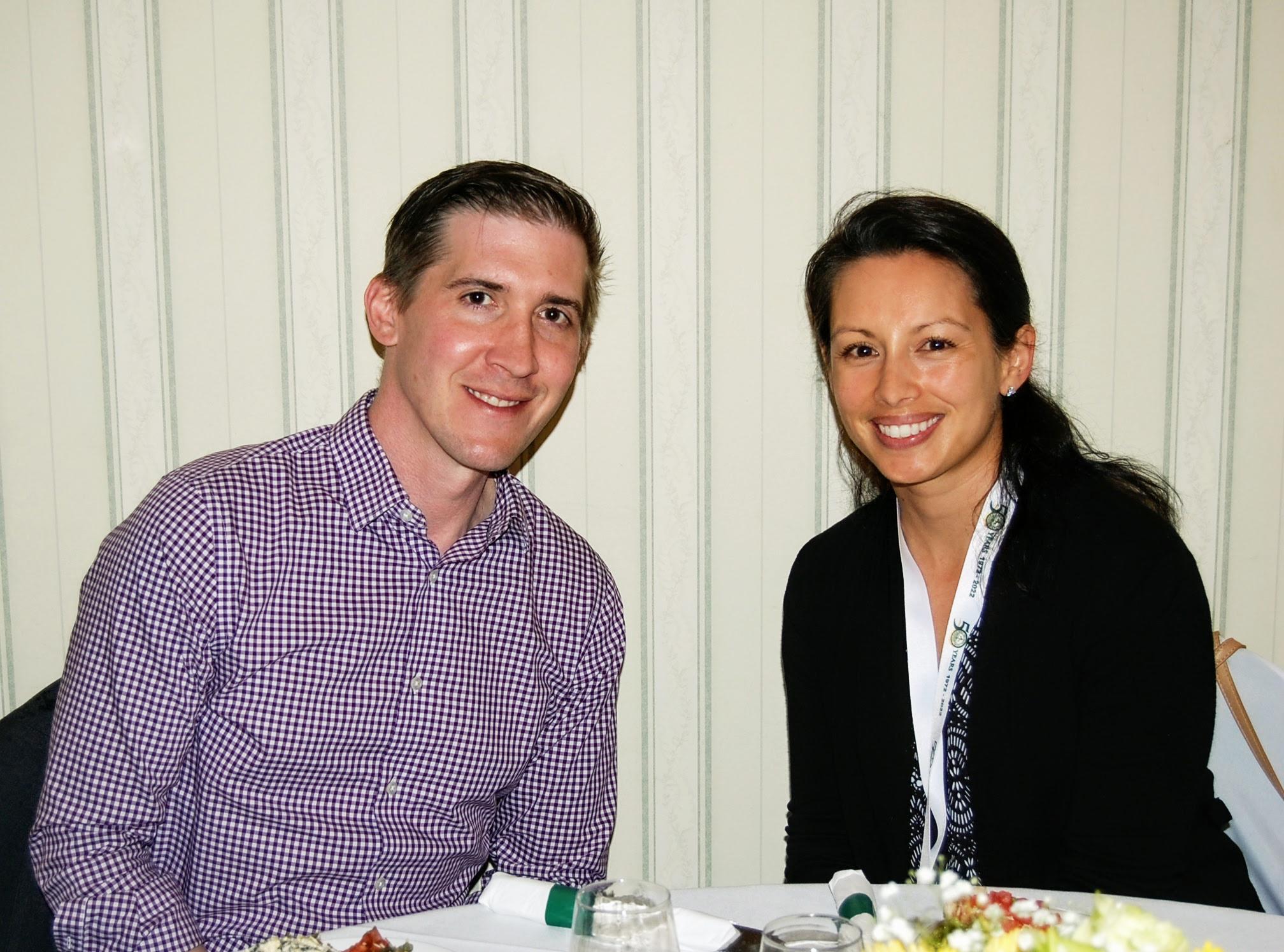 Two attendees seated at table smile at camera 