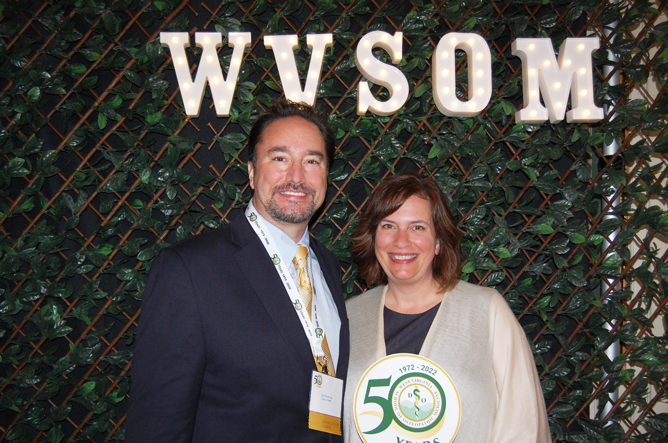 Keith Poole, DO reads the name tag on one attendee posed with another infront of WVSOM light sign