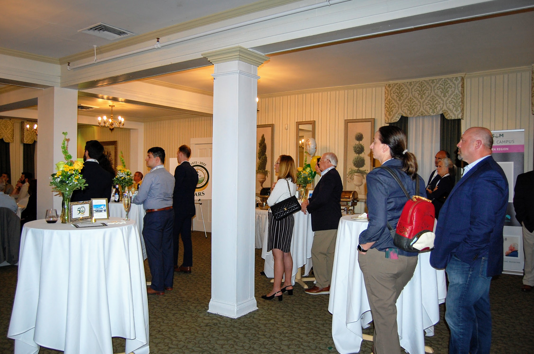 Multiple attendees at standing tables listening to event speaker