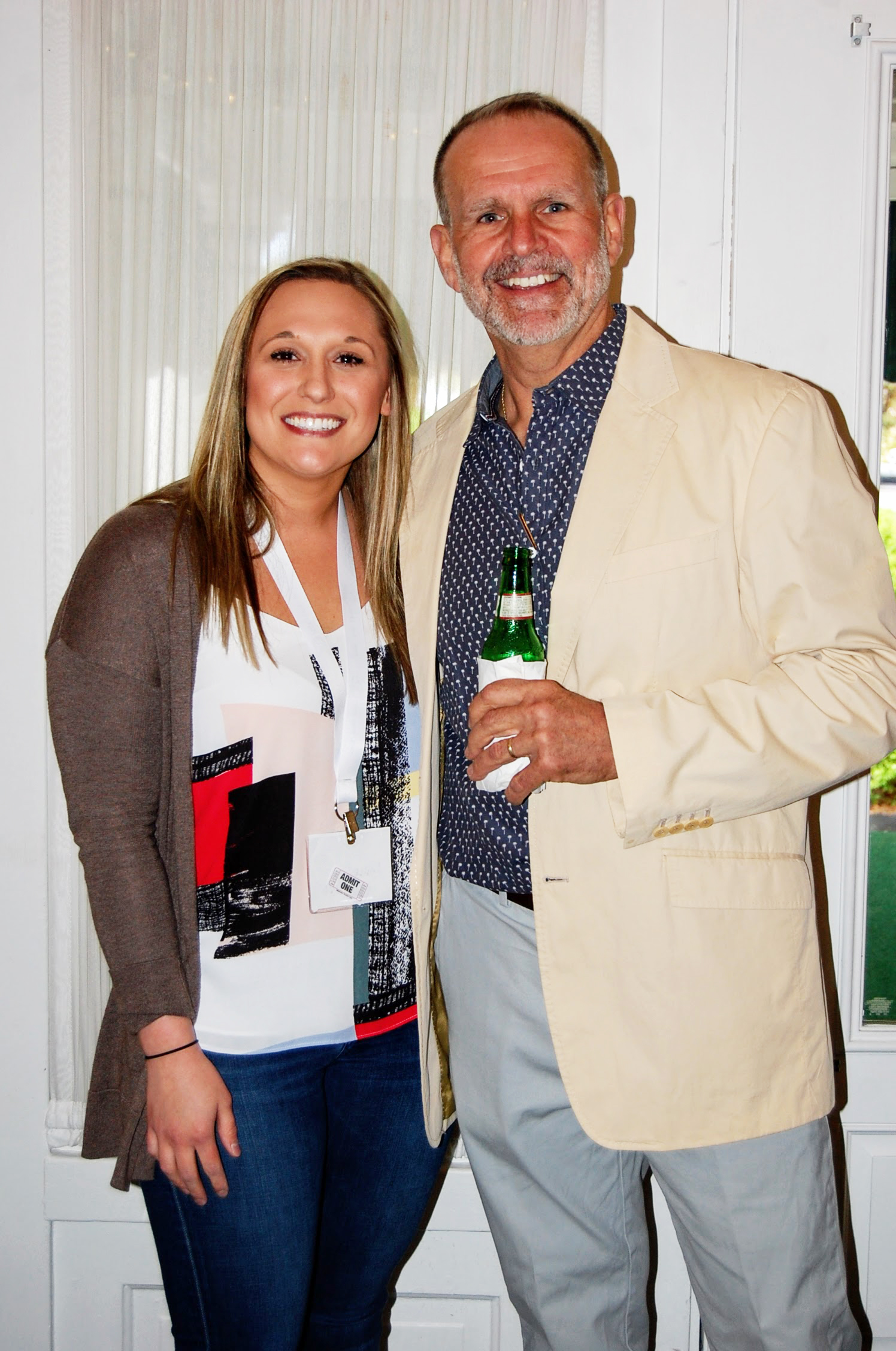 Man and woman smile for camera at event, man holds drink in hand