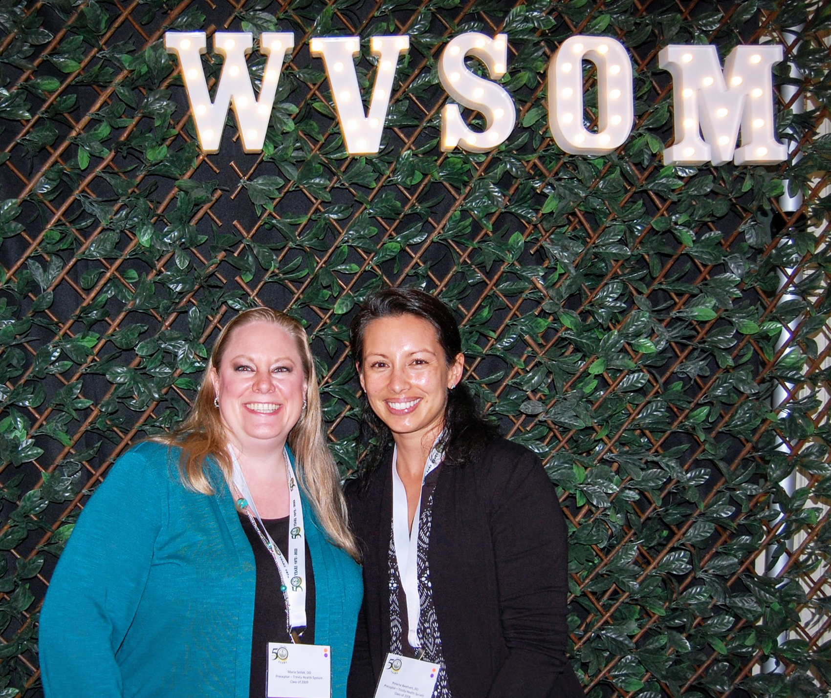 Two women pose for camera under WVSOM light sign, names on tags not visible