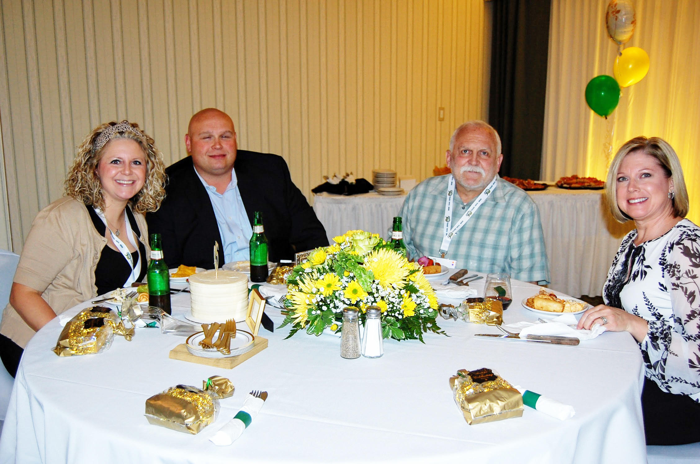 Two men and two women seated at table with food and drinks smile for camera