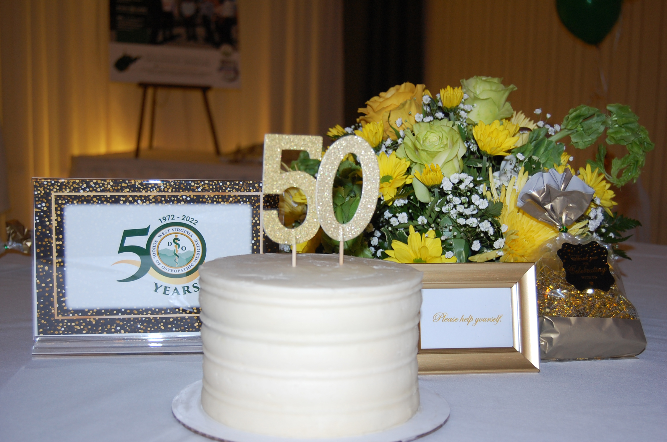 Round white cake with WVSOM 50 years decorations and flowers on table