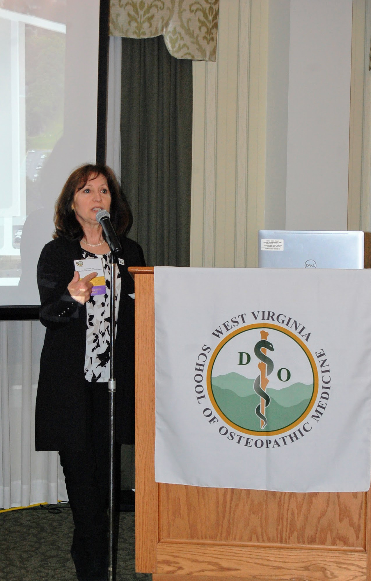 Woman speaks into microphone at WVSOM logoed podium 