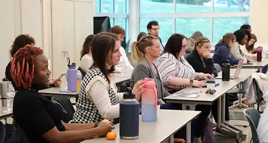 Class room of students look forward while sitting at long tables.