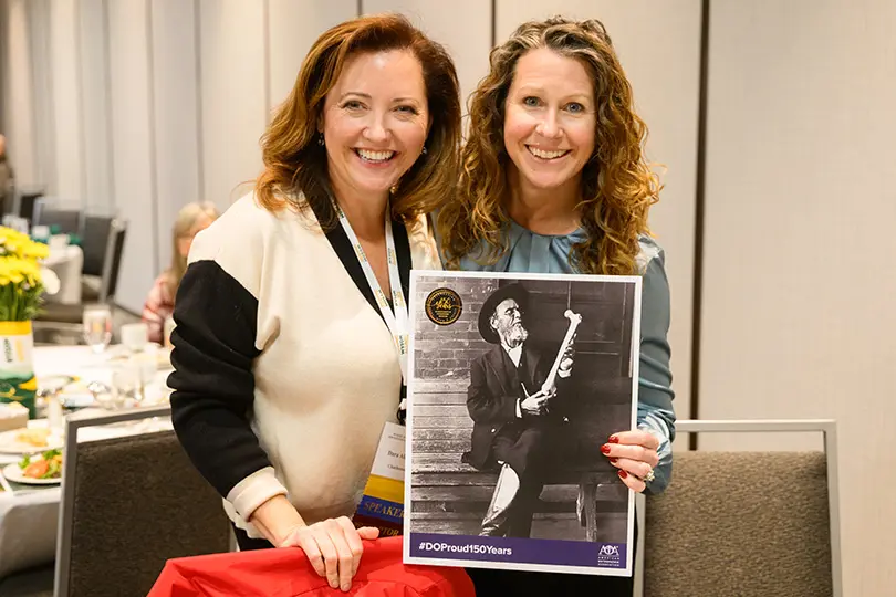 Two women smile holding picture of Osteopathic medicine founder and #DOProud150years