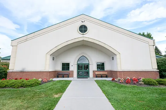Large arched entryway to building showing walkway to door, circle window inbetween entry arch and roof.
