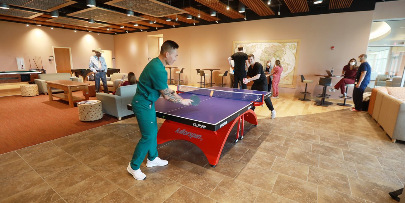 two people playing ping pong in lounge area as others mingle in background