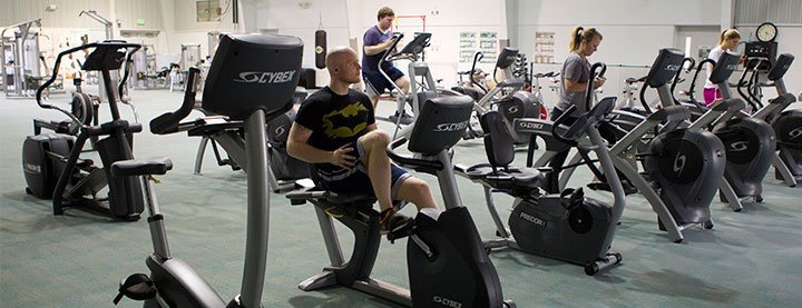 people exercising in gym on exercise bikes and elliptical machines